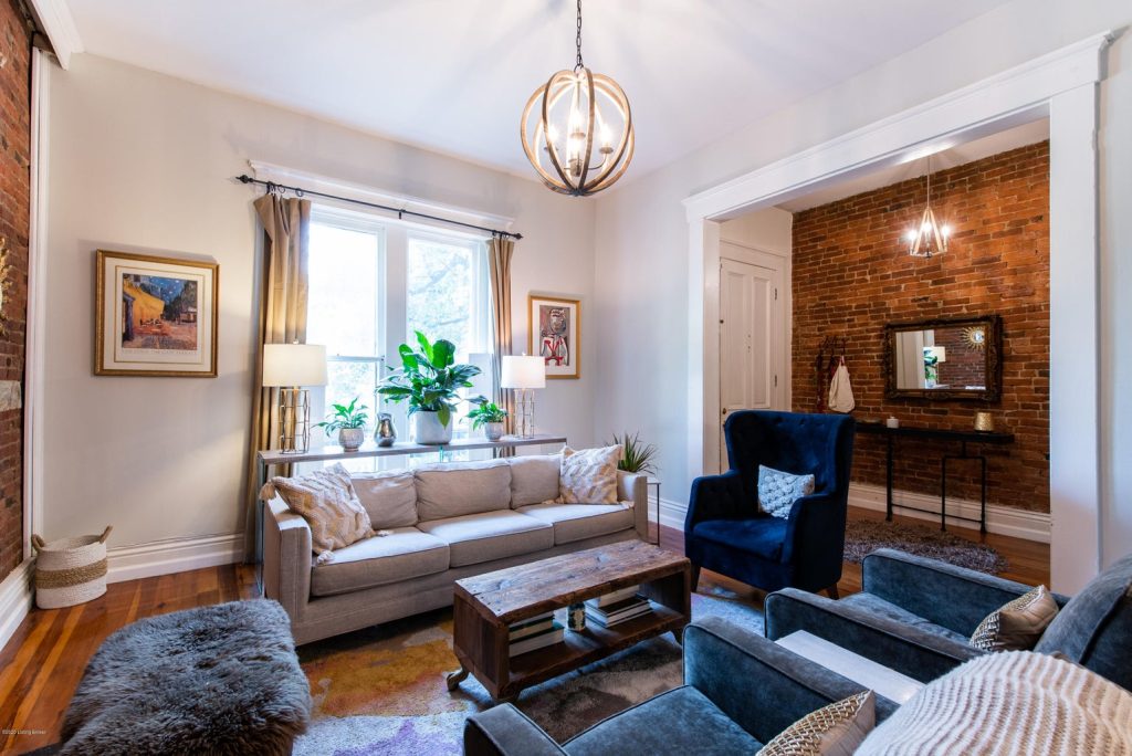 Charming living room with exposed brick walls and hardwood floors in a Butchertown home, a highlight of historic Louisville neighborhoods